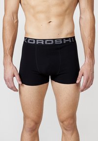 Črne bokserice z sivim elastičnim pasom, ki vsebuje ime blagovne znamke "KOROSHI." Gladko blago, prilegajoča se zasnova, dolžina do sredine stegna.