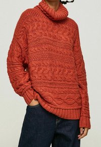 Paksu neulepusero polokauluksella poltetun oranssin sävyssä, jossa on tekstuurilliset letikuviot ja resorit hihansuissa. Yhdistetty tummiin farkkuihin.