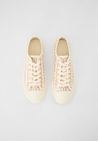Beiga kanvas sneakers med subtila logomönster, krämfärgade gummikapslar och snören, med en strukturerad yta och platt sula.