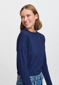 Maglietta a maniche lunghe a righe blu navy con scollo rotondo. Tessuto morbido e vestibilità comoda, abbinata a jeans di denim azzurri.