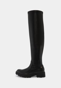 Bottes noires cuissardes en cuir lisse, avec un bout arrondi, une semelle épaisse en caoutchouc et un petit accent doré sur le talon.