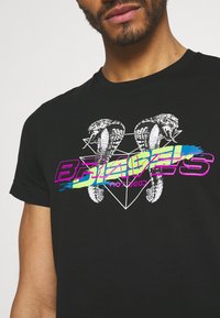 Camiseta negra con un diseño gráfico que presenta dos serpientes y una forma de diamante, acentuada por texto colorido y elementos de pinceladas.