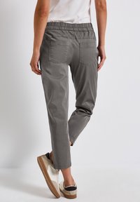 Grijze broek met elastische taille, met een taps toelopende pasvorm, twee achterzakken en een gladde textuur, gecombineerd met lichtgekleurde sneakers.