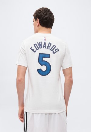 Vyras dėvi baltą sportinį marškinėlį su mėlynu užrašu „EDWARDS“ ir numeriu 5 ant nugaros, derantį su baltais šortais su juodomis juostelėmis.