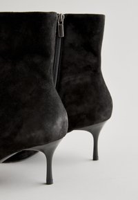 Black suede ankle boots with a high stiletto heel and a side zipper. The material is soft with a smooth texture and fitted design.