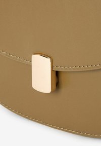 Sac rond en cuir tan avec une texture lisse, dotée d'un fermoir rectangulaire doré et d'un fil de contraste le long du bord.