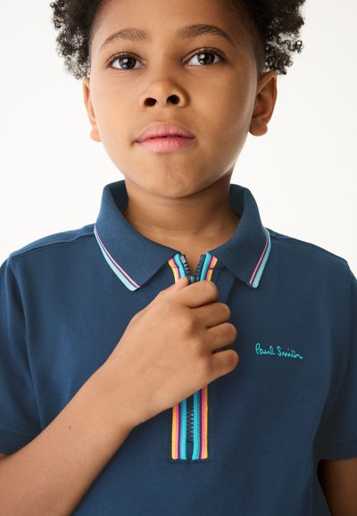 Mornarsko polo majica s kratkimi rokavi in zadrgo ovratnika, s številnimi barvnimi črtami. Vezeno ''Paul Smith'' logotip v zeleni barvi na prsih.