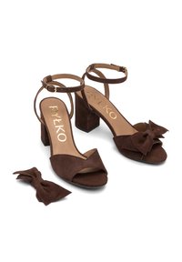 Sandali con tacco in suede marrone, con punta aperta, cinturino alla caviglia e un dettaglio a fiocco su una scarpa. Include un accessorio a fiocco abbinato. Design con tacco a blocco.