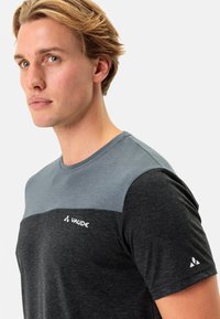 Īsām piedurknēm T-krekls ar pelēku augšējo paneli un melnu apakšējo paneli. Izgatavots no mīkstas auduma, ar baltu VAUDE logotipu un mazām akcijām.