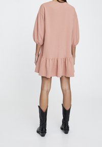 Rosa Baumwollkleid mit ausgestelltem Saum, Puffärmeln und einem lockeren Schnitt. Kombiniert mit schwarzen Stiefeln im Western-Stil.