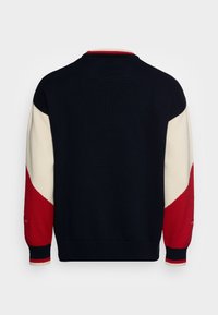 Sweter wykonany na drutach, o granatowym ciele z kremowymi i czerwonymi ukośnymi akcentami na rękawach, paskowanych mankietach oraz ściągaczu przy kołnierzu.