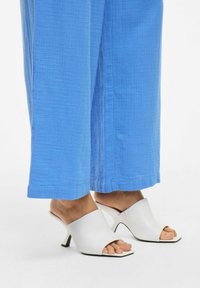 Witte open teen mules met een gebogen hak, gecombineerd met losse blauwe cropped broek van een textuur met kreukstof.