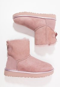 Růžové kotníkové boty z broušené kůže s krátkým nártem, měkkou podšívkou a mašlí vzadu. Podešev je texturovaná a mírně zvýšená.