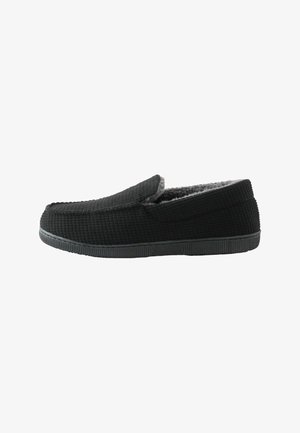 Pantofole nere a scivolo con texture, foderate in pile grigio e suola in gomma nera, mostrate in profilo verso destra su sfondo bianco.