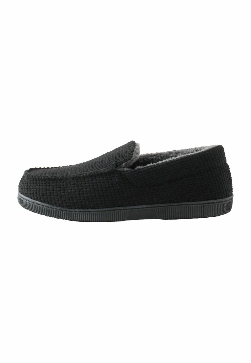 Crne teksturirane papuče na slip-on sivi krzneni uložak i crnu gumenu potplatu, prikazane u profilu okrenutom udesno na bijeloj pozadini.