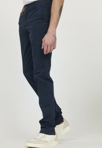 Pantalon chino en coton bleu marine avec une coupe slim, doté de poches latérales et d'une fermeture à bouton unique. Porté avec une sneaker blanche.