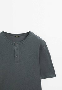 T-shirt Henley manches courtes gris foncé avec col rond et patte à trois boutons, posé à plat sur fond blanc.