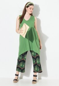 Túnica sin mangas verde, pantalones cortos negros con estampado de hojas de palmera, sandalias negras con tiras al tobillo, bolso de mano de tejido y diadema a juego.