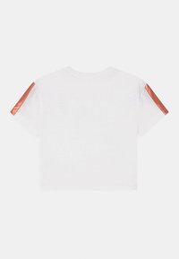 Biała krótka koszulka z krótkim rękawem, z metalicznymi miedzianymi paskami biegnącymi wzdłuż góry obu rękawów.