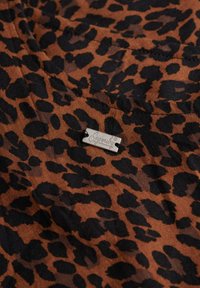 Tela de estampado de leopardo en marrón y negro con una textura suave. Presenta una pequeña etiqueta plateada con la inscripción "Superdry."