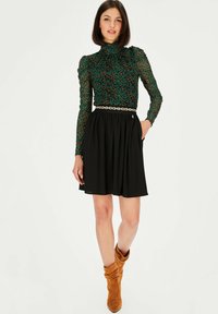 Zielono-czarna bluzka w panterkę z długimi rękawami, plisowana czarna spódnica oraz beżowe, luźne botki za kostkę. Złoty łańcuszek jako dodatek.