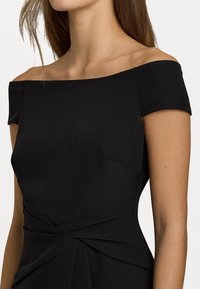 Černé šaty s odhalenými rameny, přiléhavý korzet, hladká látka, plisované detaily v pase a krátké rukávy.