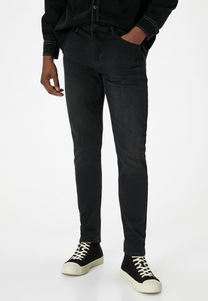 Black denim jeans with a slim fit, featuring five pockets, subtle whiskering, and contrast stitching, paired with black high-top sneakers.