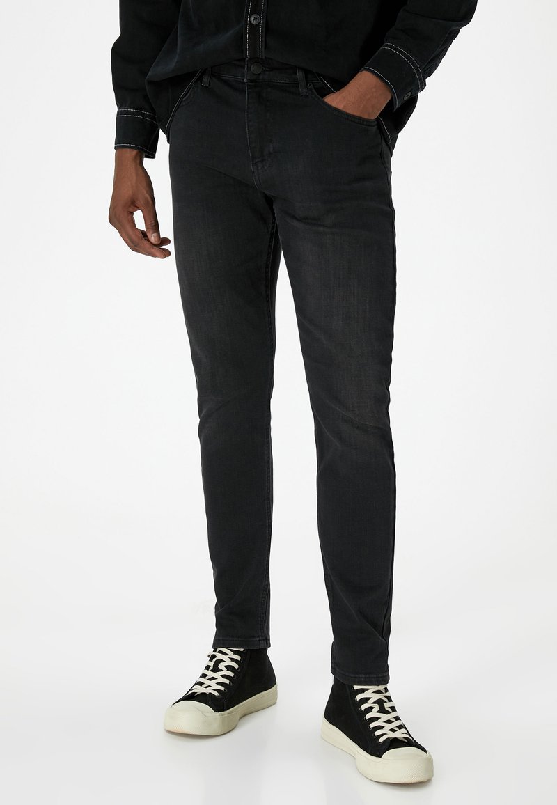 Jeans de mezclilla negra con un ajuste slim, que cuentan con cinco bolsillos, un ligero efecto desgastado y costuras en contraste, combinados con zapatillas altas negras.