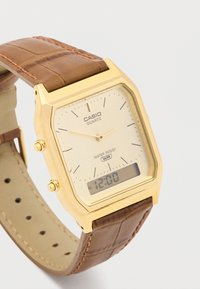 Złoty zegarek kwarcowy z kwadratową kopertą, kremową tarczą, brązowym skórzanym paskiem o teksturze krokodyla oraz wyświetlaczem cyfrowym pokazującym "12:00".