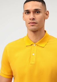 Geel polo shirt met een traditionele kraag, korte mouwen en een placket met drie knopen. De stof heeft een gladde textuur met een lichte glans.