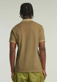 Polo shirt verde oliva a maniche corte con colletto e polsini a coste, caratterizzato da una texture liscia e un design dell'orlo dritto.