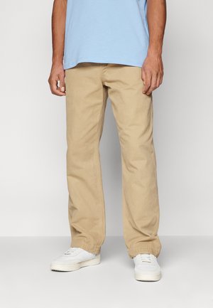 Beige cotton twill pants with a relaxed fit, straight legs, and side pockets, paired with white sneakers and a blue T-shirt.