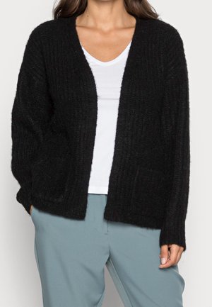 Black knitted cardigan with a V-neck, open front, and long sleeves. Features a textured pattern and two front pockets. Styled with a white top.