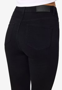 Črne denim hlače z visokim pasom, dvema zadnjima žepoma in gladko teksturo. Material je raztegljiv za udobje.