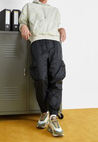 Light gray pullover hoodie with a front pocket, paired with black cargo pants featuring multiple pockets and elastic cuffs, and multicolored sneakers.