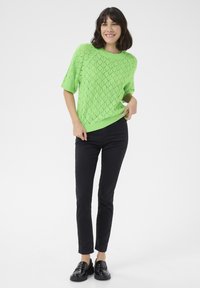 Sweter z koronkowym splotem, krótki rękaw, w jasnym zielonym kolorze, zestawiony z dopasowanymi czarnymi spodniami i czarnymi loafersami. Prosty design z fakturowanym wzorem.