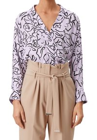 Ljuslila blus med svart blommönster, med krage och långa ärmar, tillsammans med beige högmidjade byxor och ett knytbälte.