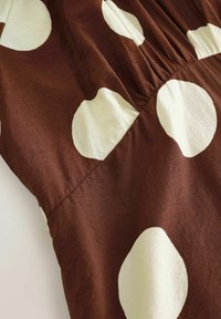 Hnedé šaty z látky s veľkými krémovými bodkami, s nariaseným pásom. Hladká textúra a jemný lesk.