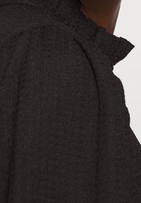 Tessuto nero con una collana arricciata. Il primo piano mette in evidenza la trama del materiale e i dettagli intricati, enfatizzando profondità e contrasto.