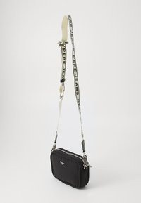 Črn tkani crossbody nahrbtnik s srebrnimi dodatki, oblazinjenim dizajnom in kontrastnim belim trakom s logotipom "PEPE JEANS". Zadrga za zapiranje.