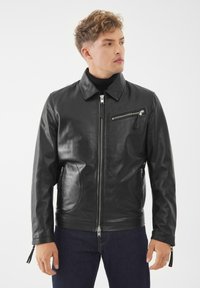 Černý kožený kabát s líme�čkem, předním zipem a bočními kapsami na zip. Obsahuje kapsu na zip na hrudi a texturovanou úpravu.