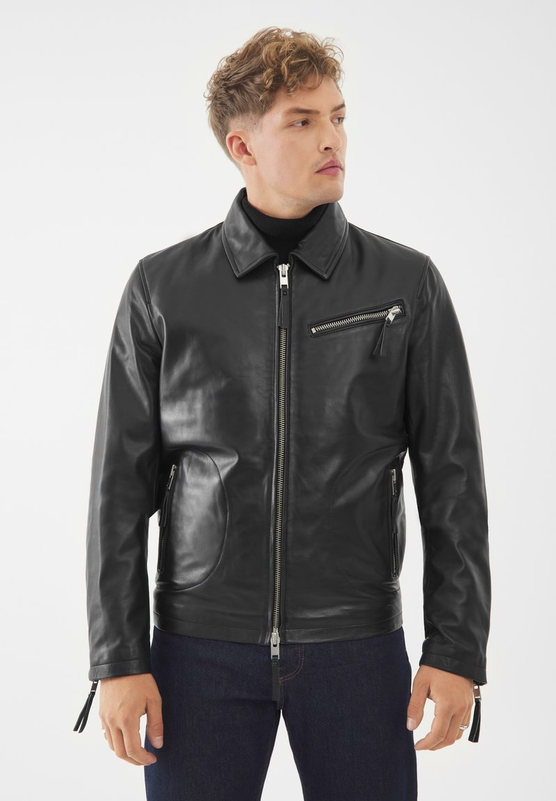 Černý kožený kabát s límečkem, předním zipem a bočními kapsami na zip. Obsahuje kapsu na zip na hrudi a texturovanou úpravu.