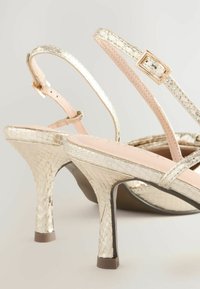 Sandales à talons hauts dorées métalliques avec un motif en relief de peau de serpent, dotées de fines lanières, d'une boucle carrée et d'une semelle intérieure rose.