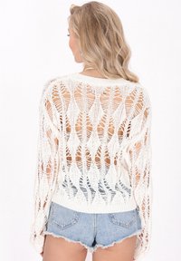 Maglione bianco lavorato a maglia con una trama larga e aperta a rombi, dotato di maniche lunghe e orlo a costine, abbinato a un paio di pantaloni shorts di jeans.
