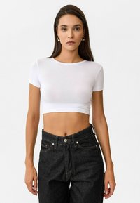 Witte, korte mouwen cropped t-shirt van lichtgewicht stof, gecombineerd met hoog getailleerde zwarte denim jeans met zichtbare stiksels en knoopsluiting.