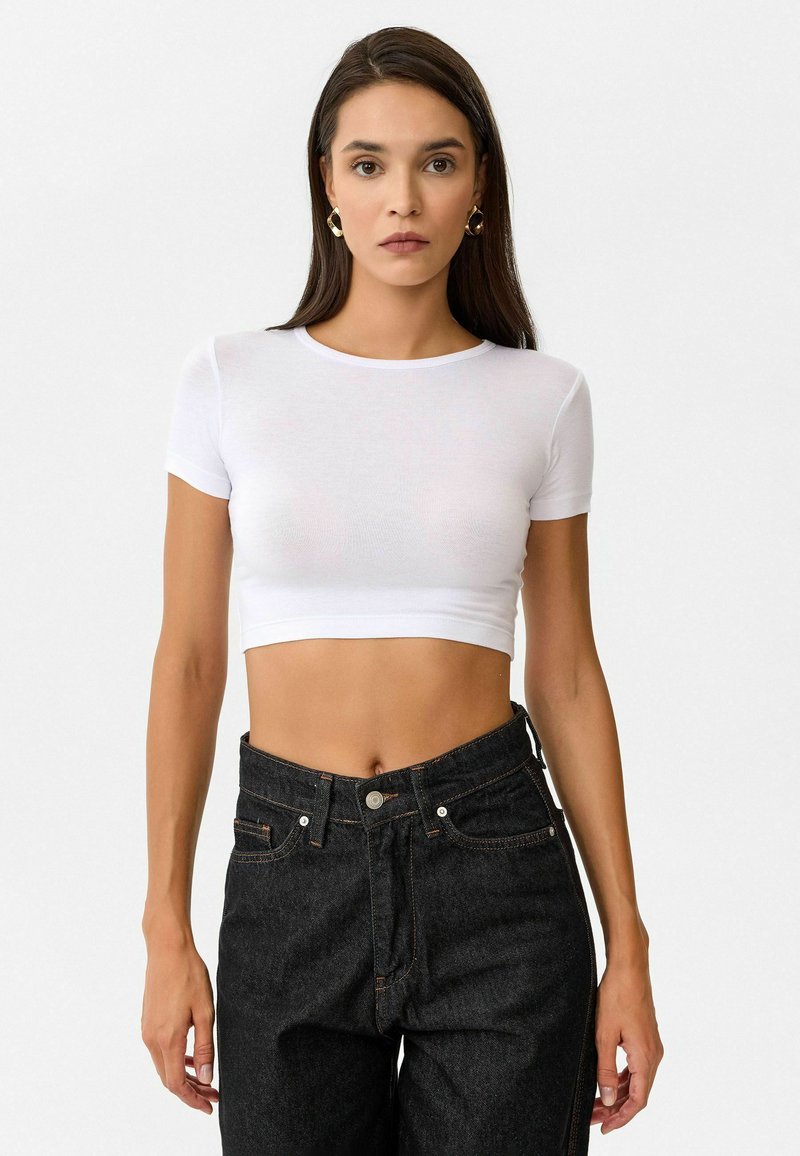 Witte, korte mouwen cropped t-shirt van lichtgewicht stof, gecombineerd met hoog getailleerde zwarte denim jeans met zichtbare stiksels en knoopsluiting.
