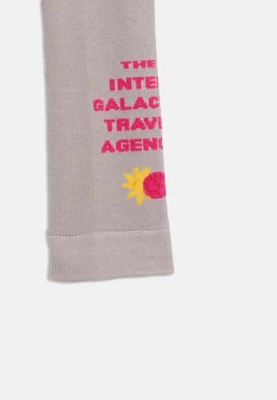 Lysegrå sokk med rosa tekst som sier "THE INTERGALACTIC TRAVEL AGENCY" og en liten gul og rosa solgrafikk nær mansjetten.
