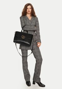 Borsa a tracolla in pelle nera con manico superiore e tracolla removibile, dotata di una chiusura in metallo dorato. Completo in tessuto grigio testurizzato.