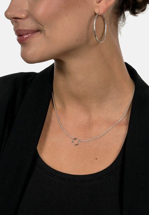 Silberne Creolen und eine zarte Silberkette mit einem kleinen, runden Akzent, getragen mit einem schwarzen Oberteil und Blazer.