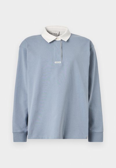 Camisa polo de manga larga azul claro con un cuello blanco contrastante, que presenta una tapeta frontal discreta y una pequeña etiqueta en el escote.